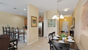 A dining area with a table set for four, surrounded by chairs, with a kitchen in the background. - Paradise Palms 8978 (Kissimmee)