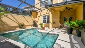 A swimming pool with a glass ceiling, surrounded by potted plants and a patio area with a ceiling fan. - Paradise Palms 8978 (Kissimmee)