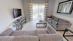 A modern living room with a sofa set, a coffee table, a TV, and a dining area with a table and chairs. - Encore Resort at Reunion 361 (Kissimmee)