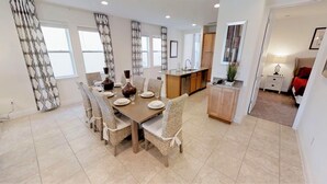 A dining area with a large table set for six, surrounded by wicker chairs. There is a kitchen area with wooden cabinets and a countertop visible in the background. - Encore Resort at Reunion 361 (Kissimmee)