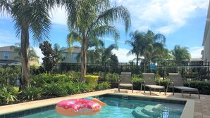 A clear swimming pool with a pink inflatable donut float, surrounded by palm trees and a fence. - Encore Resort at Reunion 361 (Kissimmee)
