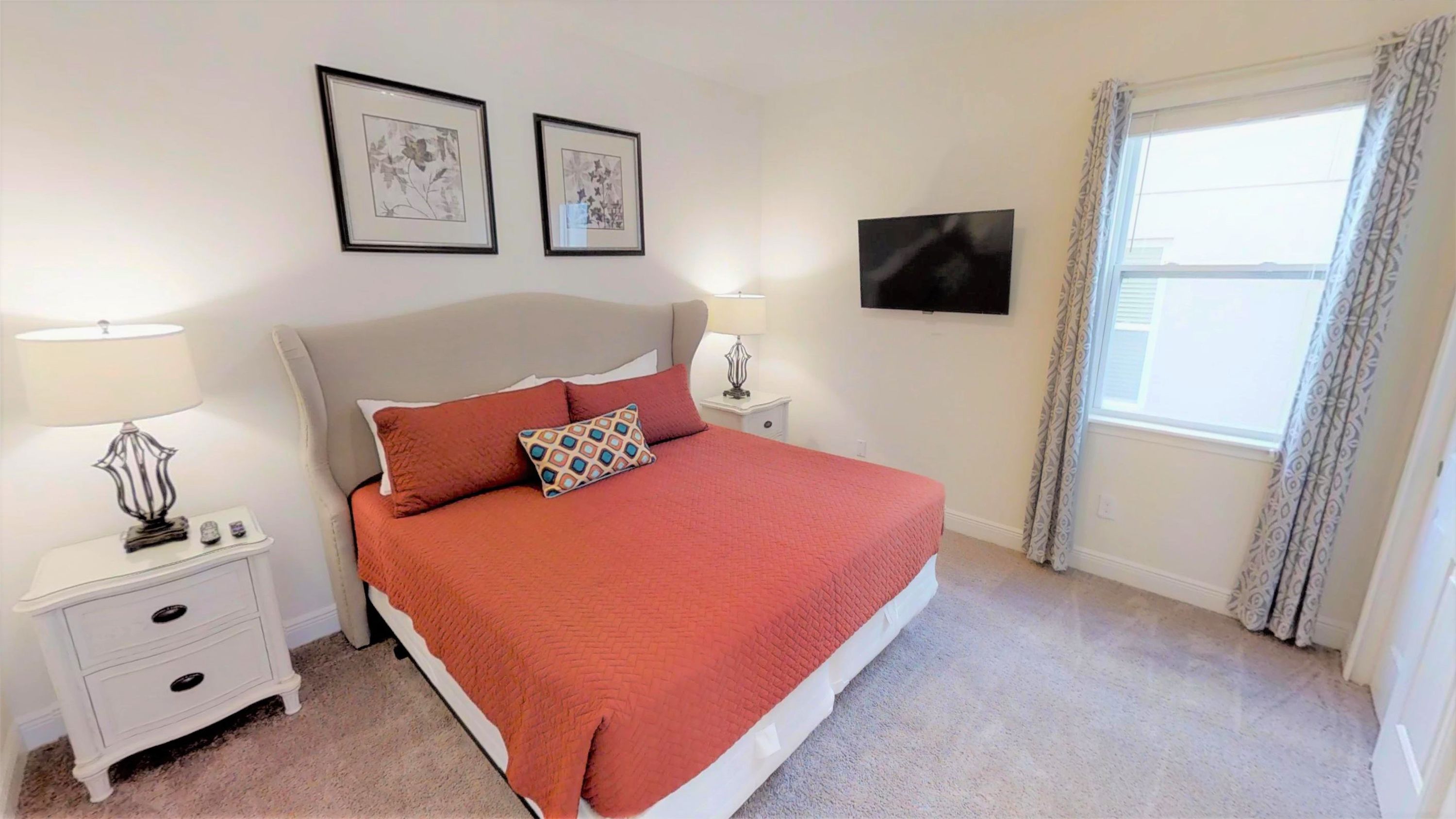 A neatly arranged bedroom with a large bed, two bedside tables, a flat-screen TV, and two framed pictures on the wall.