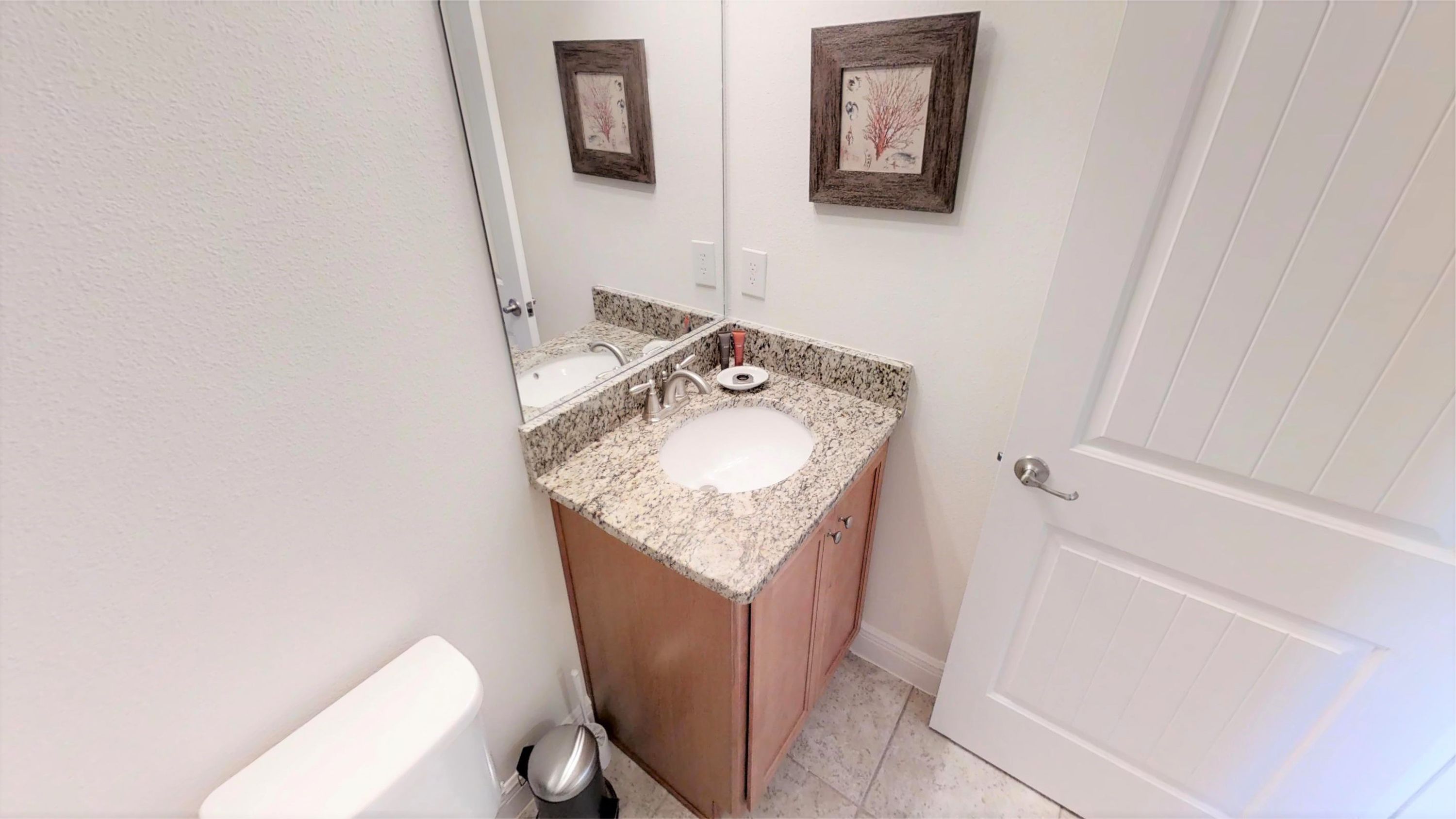 A bathroom with a white sink, granite countertop, wooden cabinets, a toilet, and a door.