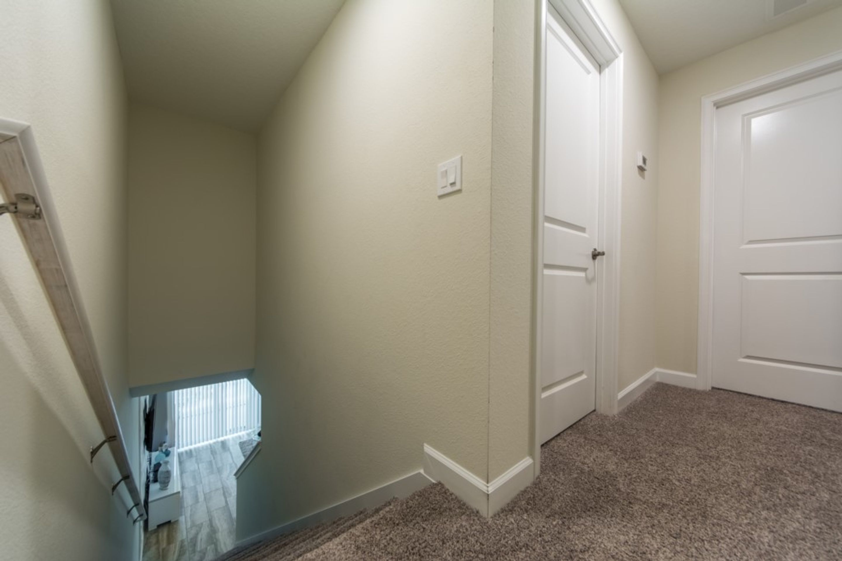 A hallway with carpeted flooring, white walls, and a door at the end.