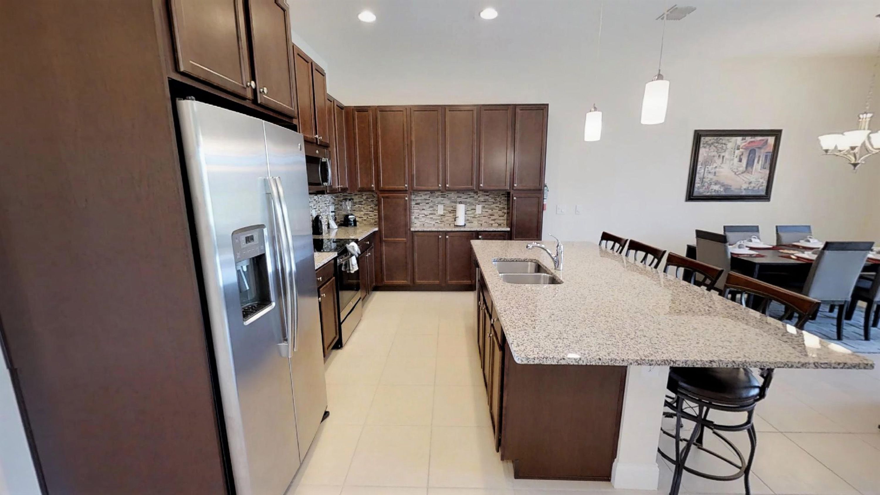 A modern kitchen with dark wood cabinets, stainless steel appliances, a granite countertop, and a dining area with chairs and a table.