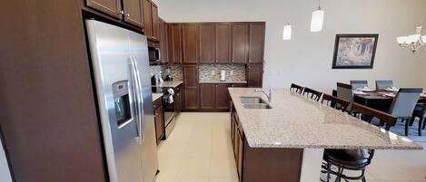 A modern kitchen with dark wood cabinets, stainless steel appliances, a granite countertop, and a dining area with chairs and a table.
