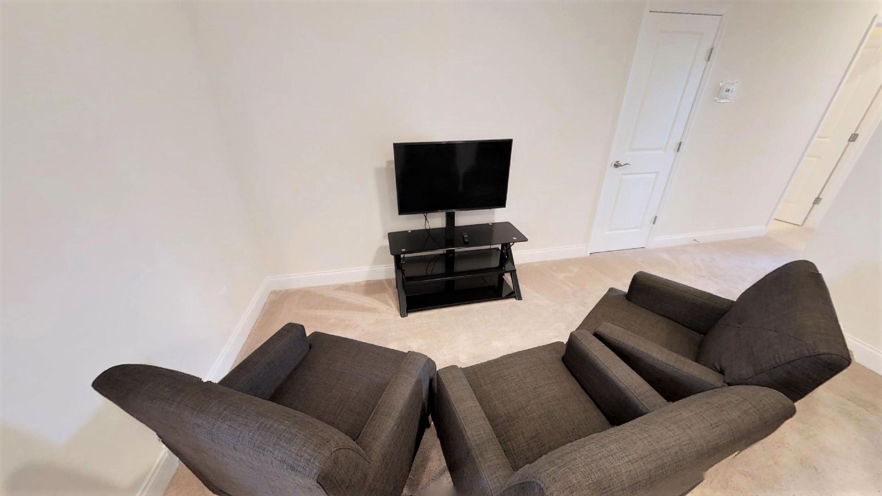 A living room with a flat-screen TV on a black stand, two grey sofas, and a white door in the background.