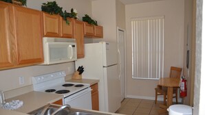 A compact kitchen with wooden cabinets, a microwave, a stove, a refrigerator, and a dining area with a table and chairs. - Regal Palms Resort & Spa 2000 (Davenport)