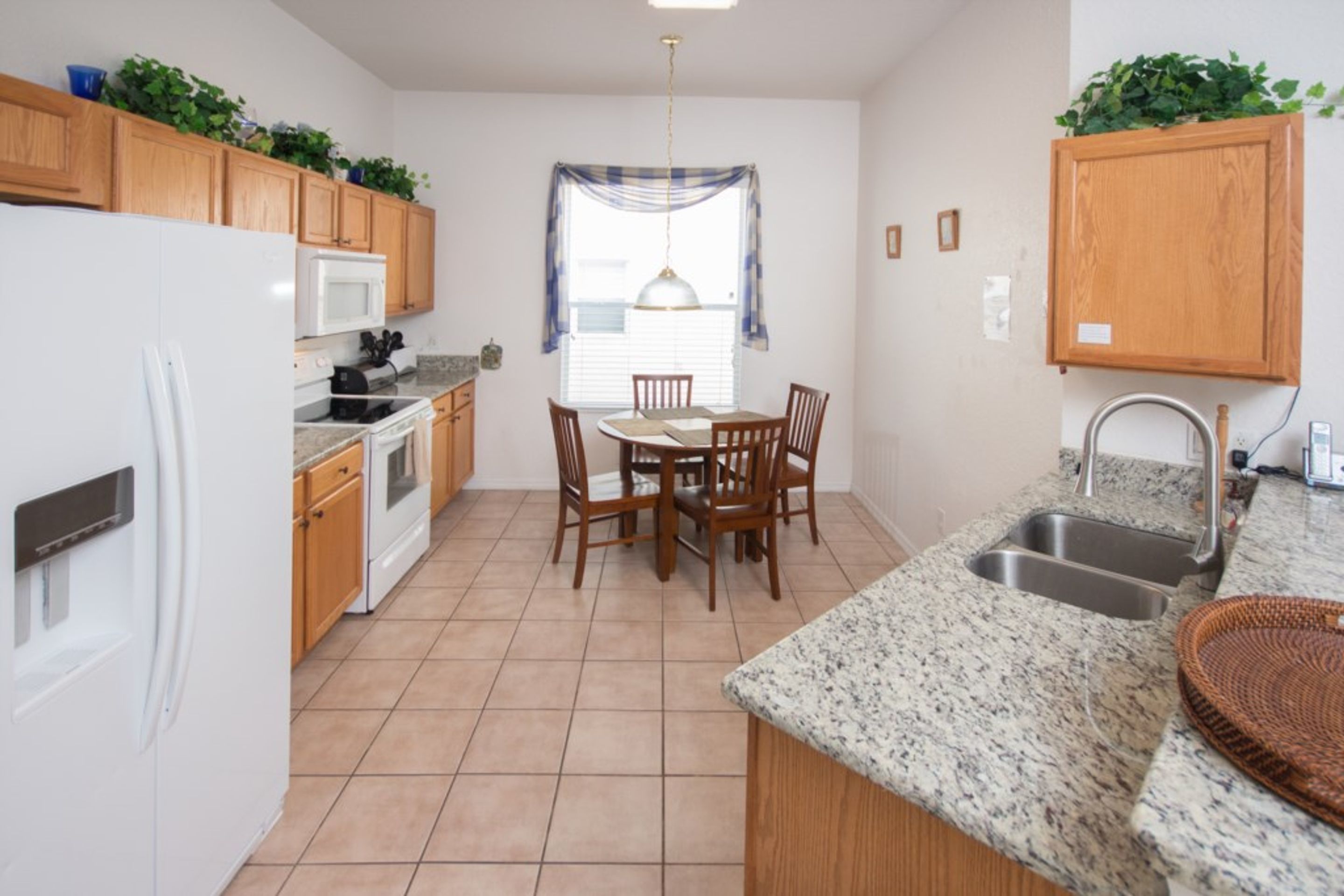 A compact kitchen with wooden cabinets, a white refrigerator, a microwave, a stove, a dining table with chairs, and a sink.
