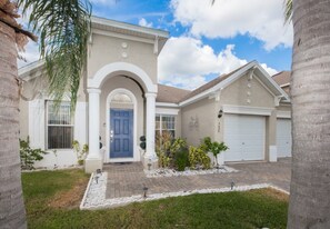 A two-story house with a blue front door, a garage, and a landscaped front yard with palm trees and shrubs.