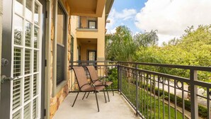 A balcony with two chairs, a door with blinds, and a view of a street and greenery. - Bella Piazza 903 - 827 (Davenport)