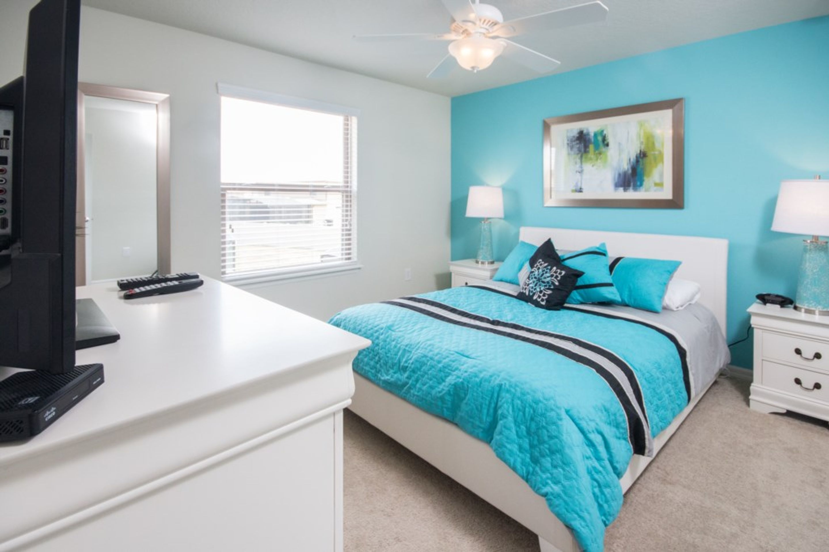 A bedroom with a bed, a desk, a television, and a window.