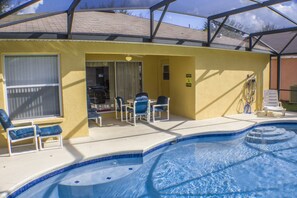 A pool area with a hot tub, lounge chairs, and a covered patio.