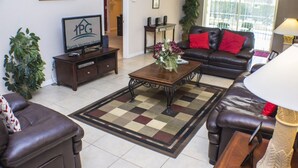 A living room with a brown leather sofa, a coffee table, a TV on a stand, and a large window with a view of the outside. - Silver Creek 1435 (Clermont)