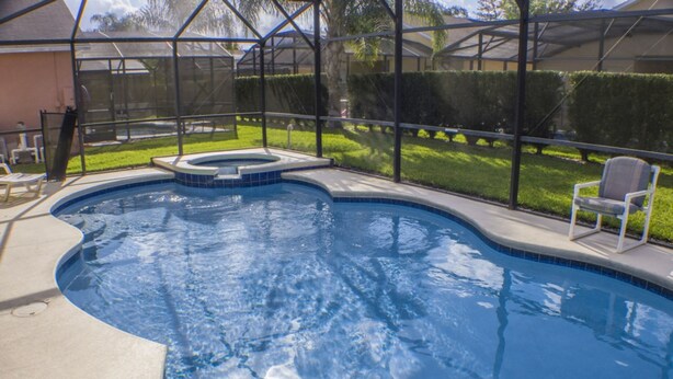 A swimming pool with a built-in hot tub, surrounded by a covered patio area with chairs. - Silver Creek 1435 (Clermont)