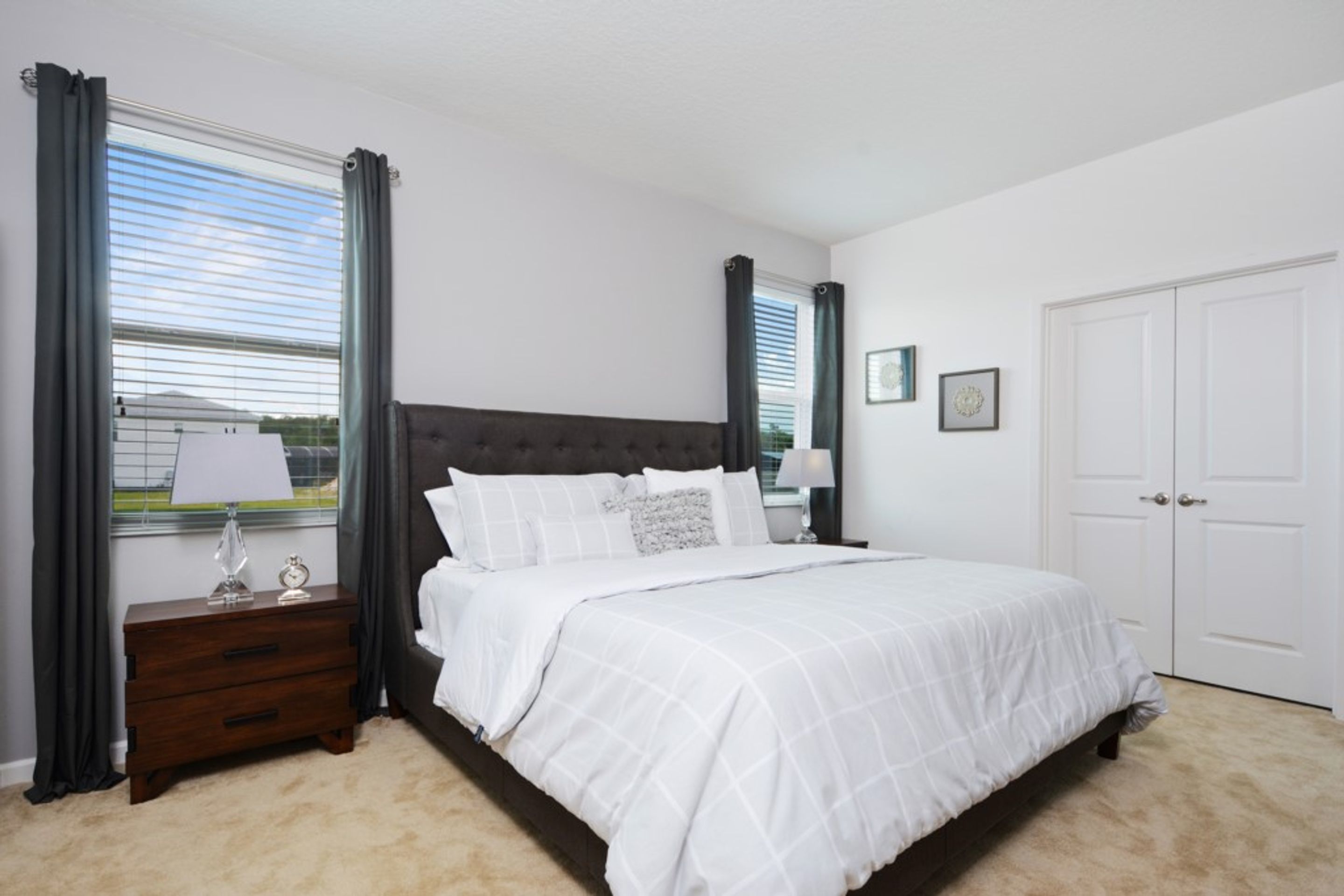 Une chambre à coucher avec un grand lit, une table de chevet, une commode et une fenêtre avec des rideaux.