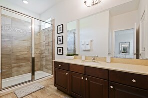 A modern bathroom with a glass shower enclosure, a large mirror, dark wooden cabinets, and a beige countertop.
