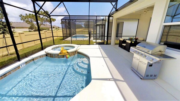 A swimming pool with a hot tub, a barbecue grill, and a covered patio area.