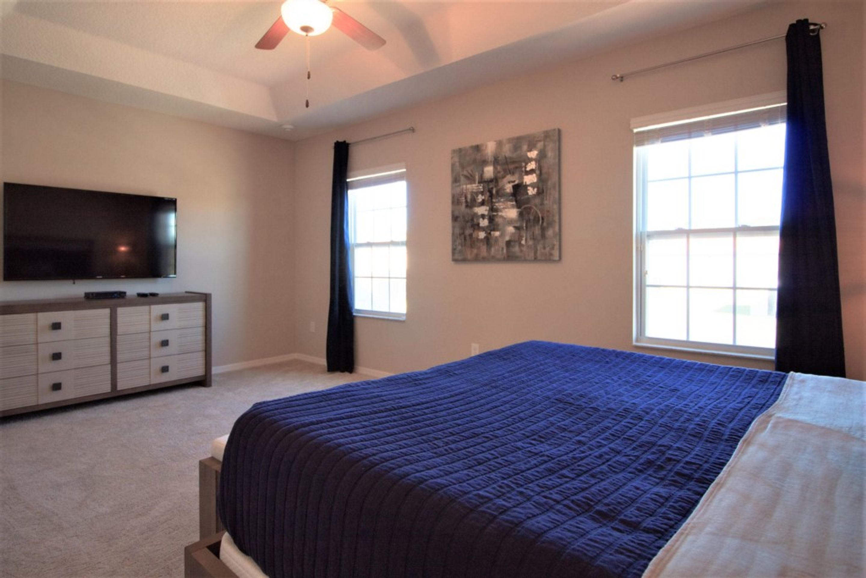 A bedroom with a bed, a television on a dresser, and a ceiling fan.