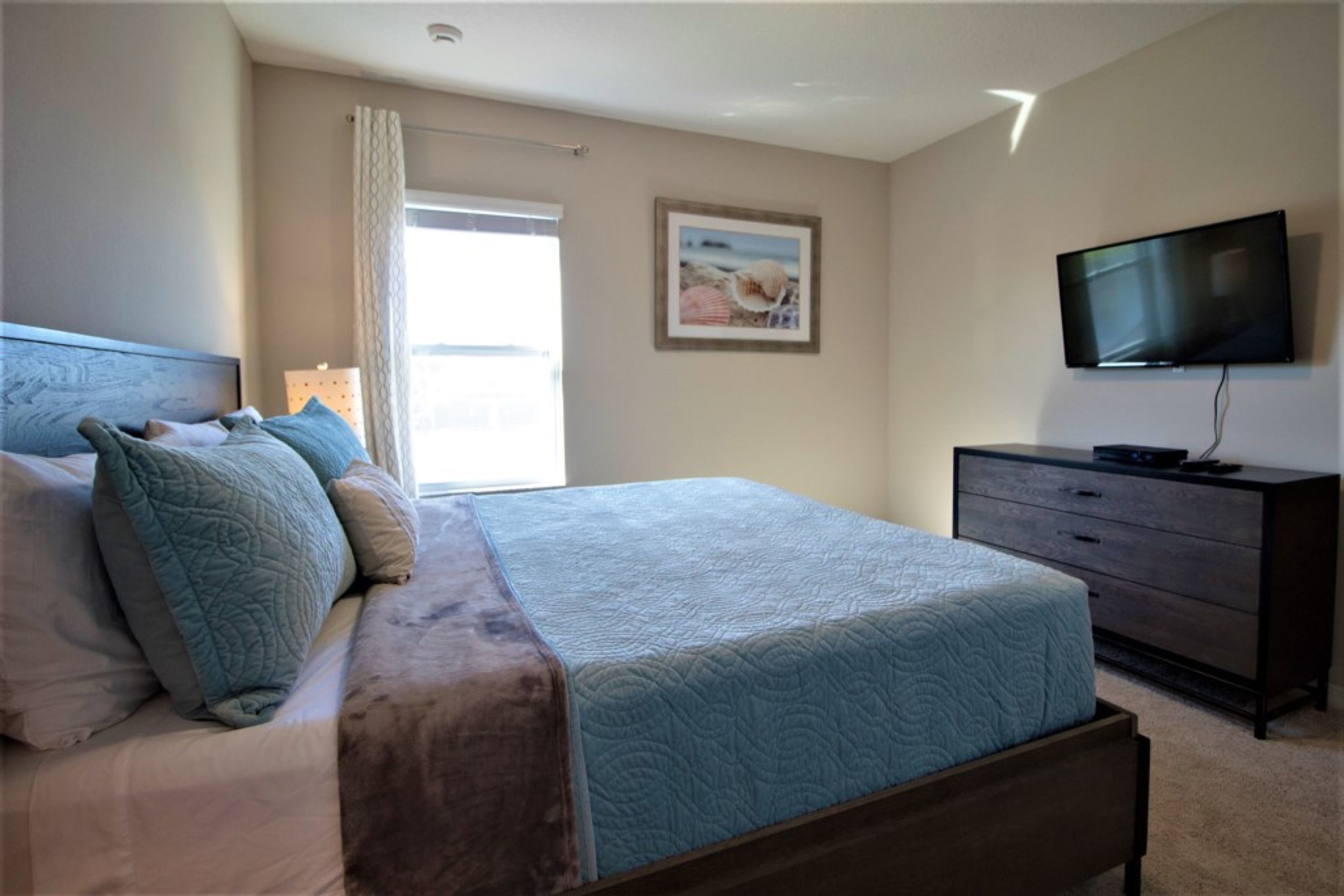 A bedroom with a bed, a dresser, a television, and a window with curtains.