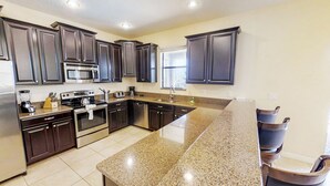 A modern kitchen with dark wood cabinets, stainless steel appliances, and a granite countertop. - Champions Gate 9035 (Davenport)
