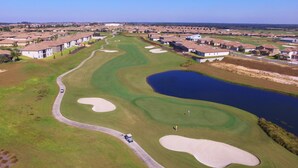 An aerial view of a golf course with sand bunkers, a pond, and residential buildings in the background. - Champions Gate 9035 (Davenport)