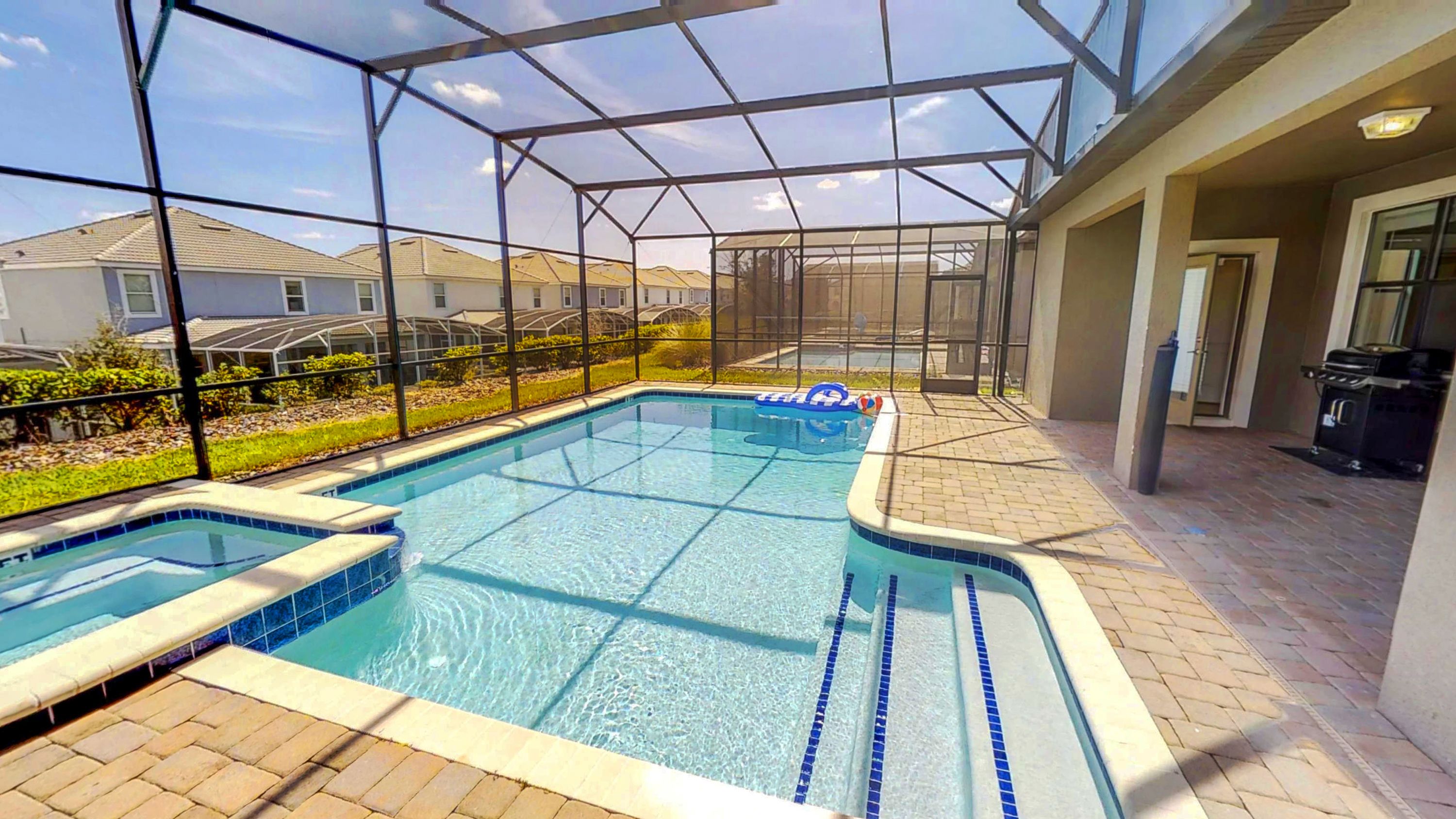 Ein Swimmingpool mit Glasveranda, umgeben von einer Terrasse mit Grill.