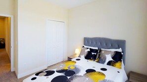 A bedroom with a bed, a nightstand, a lamp, and a door.