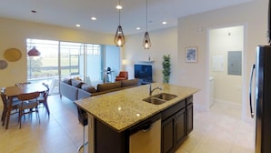Una cocina moderna con una isla central, comedor con sillas, un sofá y un televisor.