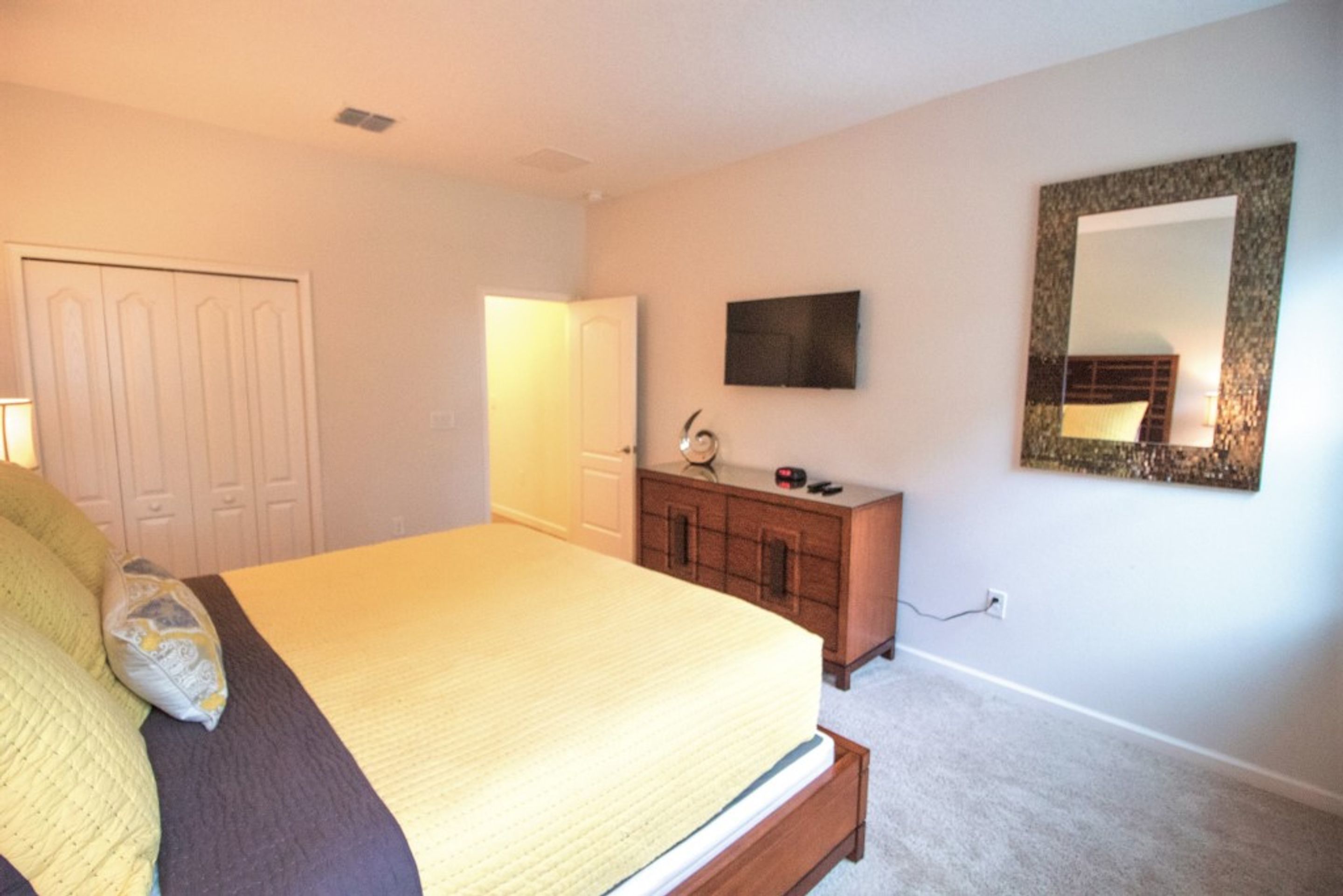 Une chambre à coucher avec un lit, une commode, une télévision et un miroir au mur.