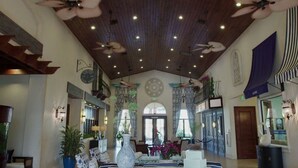 Un lobby amplio con techo alto, ventiladores de techo y un área de estar central con un jarrón grande y plantas en macetas.
