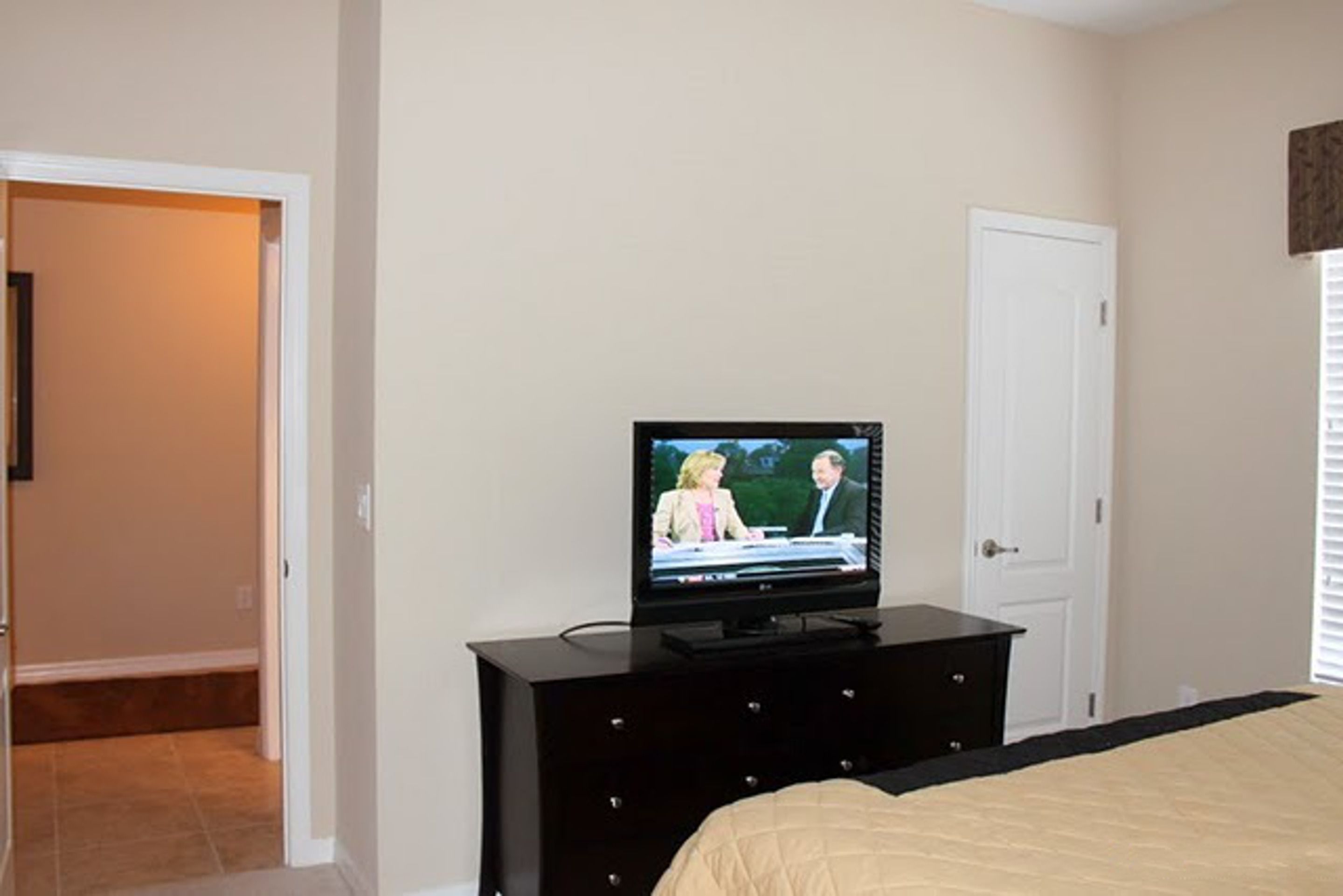 A bedroom with a TV on a dresser, a bed, and a door.
