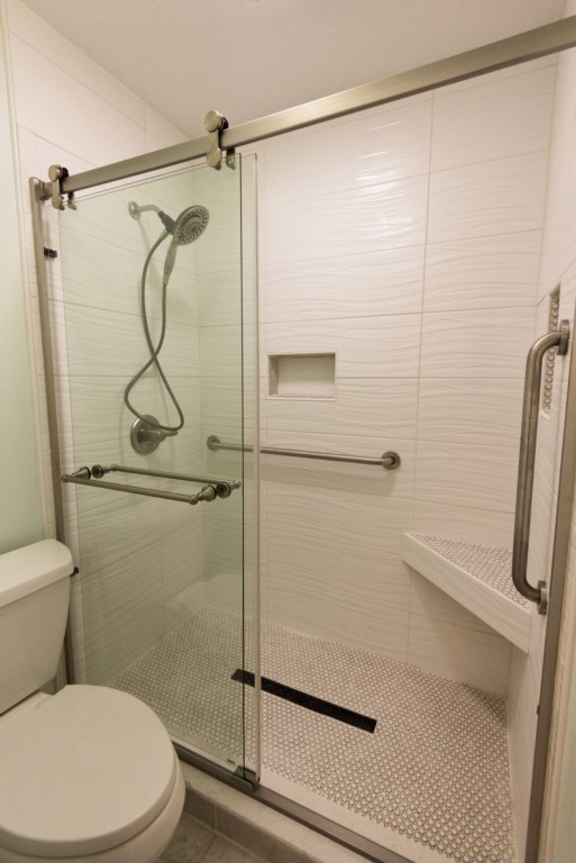 Ein Duschbereich mit Glaswänden, Toilette und einer Haltestange.