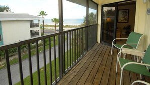 Un balcon en bois avec deux chaises vertes, une vue sur la plage et une maison en arrière-plan.