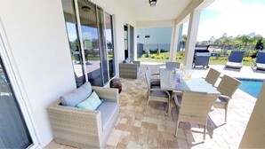 A covered patio area with wicker furniture, a glass table, and a pool in the background. - Encore Resort at Reunion 7632 (Kissimmee)