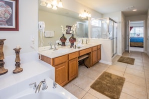 A modern bathroom with a large mirror, two sinks, wooden cabinets, and a bathtub.