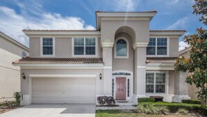 A two-story house with a white garage door, a central arched entrance, and a tiled roof. - Windsor Hills 2548 (Kissimmee)