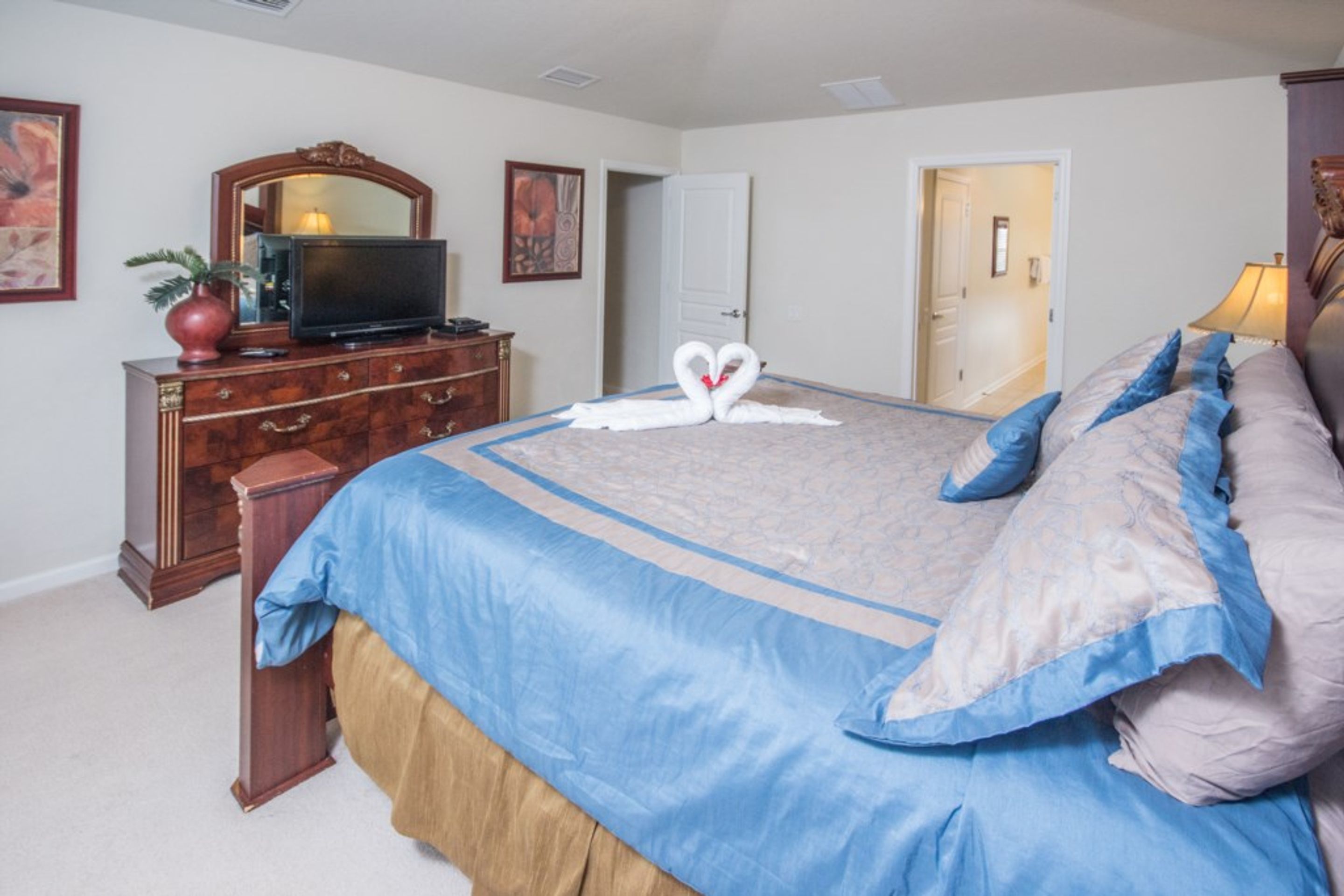 Une chambre à coucher avec un grand lit, une commode, un téléviseur et une porte donnant sur une autre pièce.