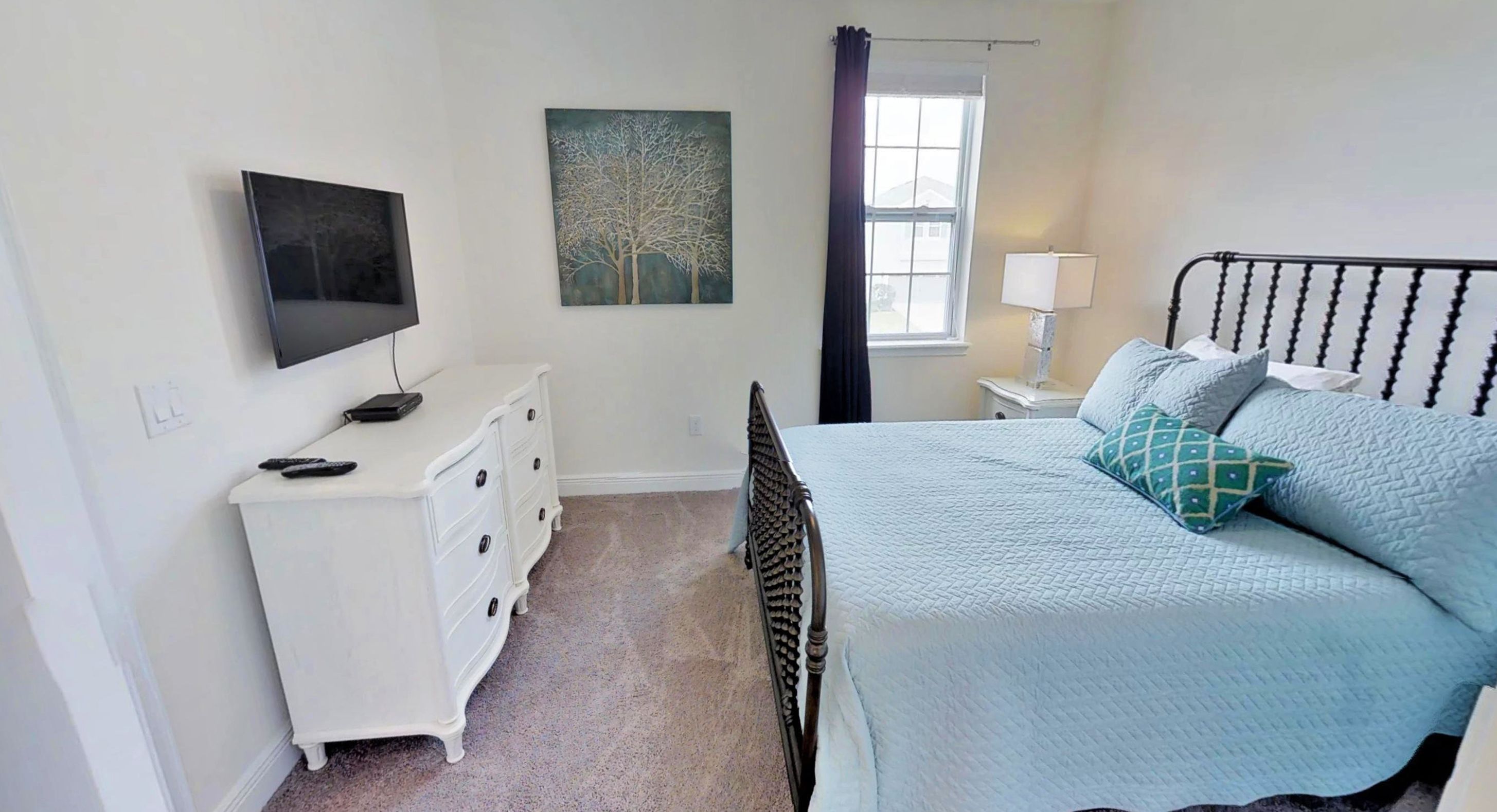 A bedroom with a bed, dresser, TV, and artwork.