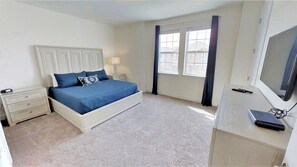 A bedroom with a bed, a nightstand, a desk with a computer, and a window with curtains. - Encore Resort at Reunion 7521 (Kissimmee)