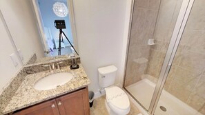 A bathroom with a granite countertop sink, a toilet, and a glass shower enclosure. - Encore Resort at Reunion 7521 (Kissimmee)