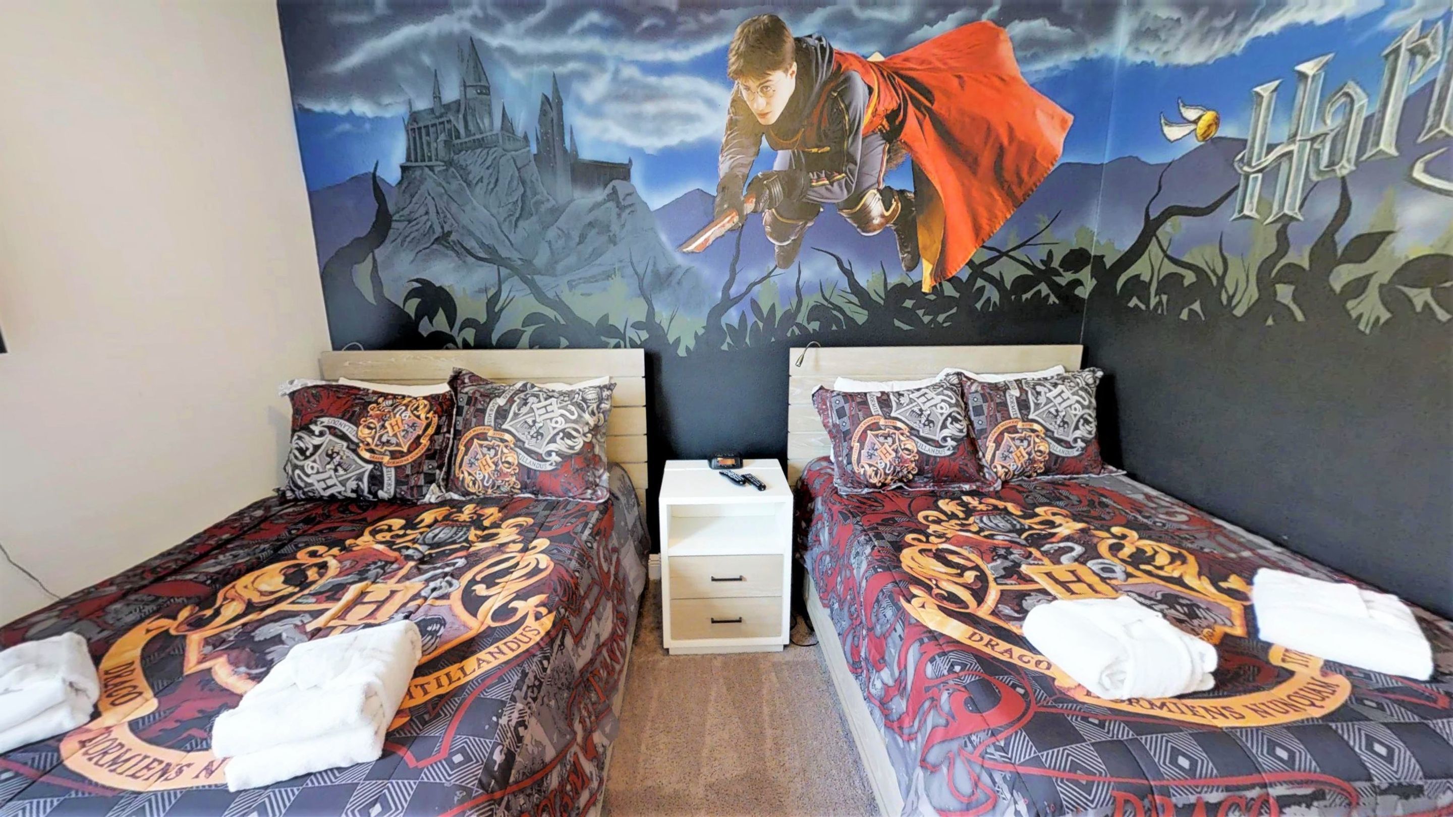 Huoneessa on kaksi sänkyä, joissa kummassakin on Harry Potter -teemainen päiväpeite, sänkyjen välissä yöpöytä sekä seinällä suuri seinämaalaus, jossa on kuvattuna linna ja hahmo taustalla.