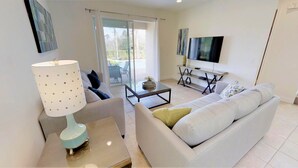 A modern living room with a sofa, a coffee table, a TV, and a sliding glass door leading to an outdoor area. - Encore Resort at Reunion 7521 (Kissimmee)