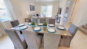A dining area with a table set for four, surrounded by chairs, and a sofa in the background. - Encore Resort at Reunion 7521 (Kissimmee)