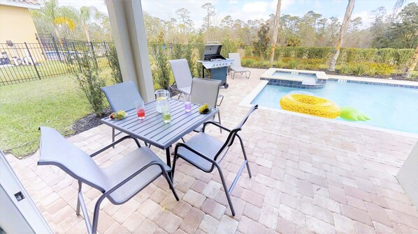 An outdoor patio with a pool, a grill, and a table with chairs. - Encore Resort at Reunion 7521 (Kissimmee)