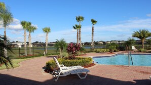 A pool area with palm trees, a brick pathway, and lounge chairs. - Crystal Cove 947 (Kissimmee)