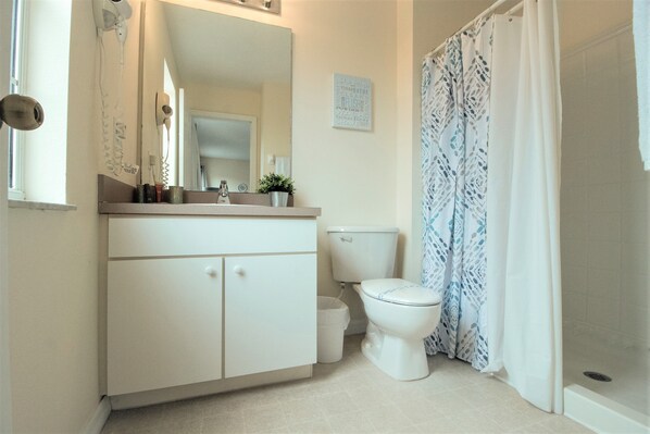 Un baño con lavamanos blanco, espejo, inodoro y cortina de ducha.