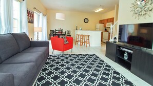 A living room with a grey sofa, a red chair, a black and white patterned rug, a TV, and a kitchen area with a microwave and a refrigerator. - Terra Verde Resort 101 (Kissimmee)