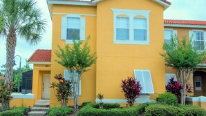A yellow building with white shutters, numbered 101 and 103, surrounded by greenery and a palm tree. - Terra Verde Resort 101 (Kissimmee)