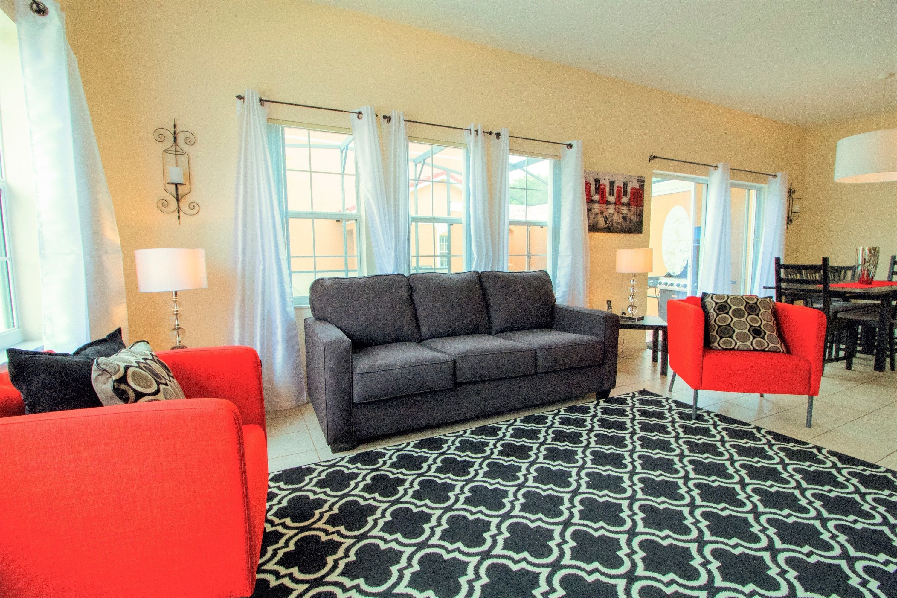 Una sala de estar con un sofá gris, un sillón rojo y una alfombra estampada.